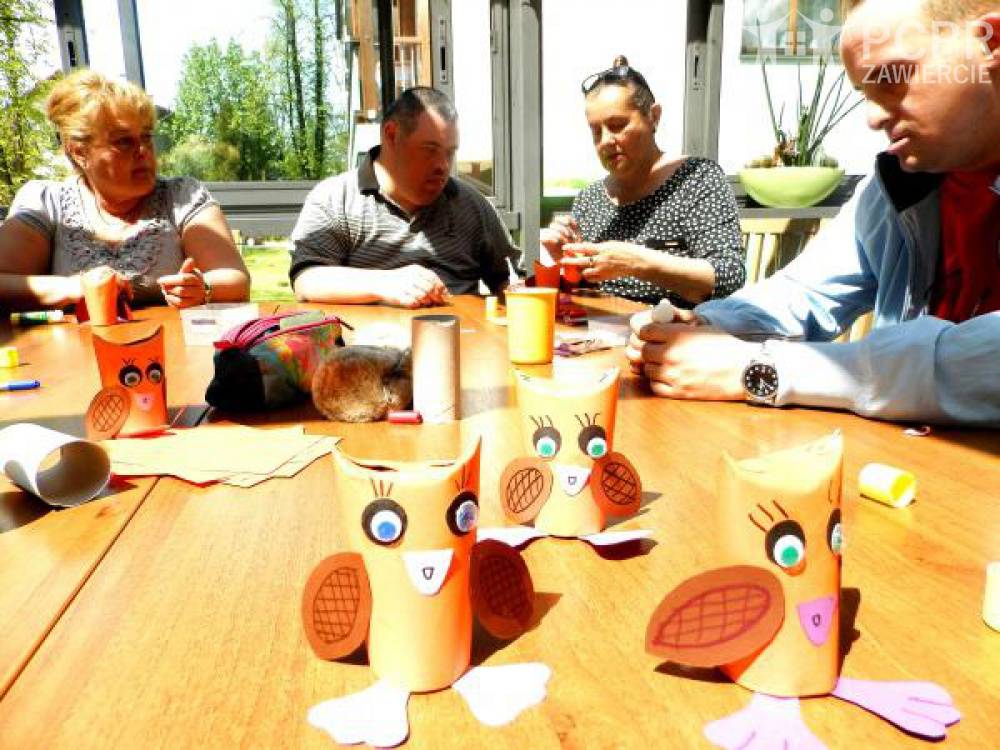 Zdjęcie: Grupa kobiet i mężczyzn przy stole wykonuje sowy z papieru